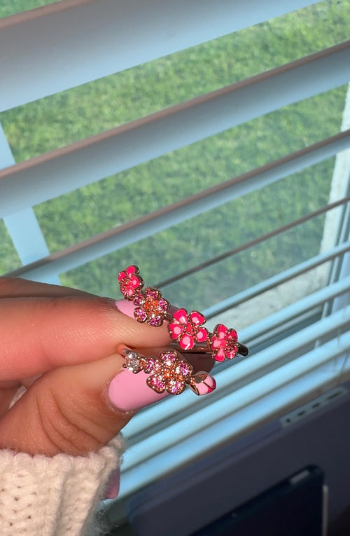 Hand holding a pink floral hair clip with a blurred green outdoor background